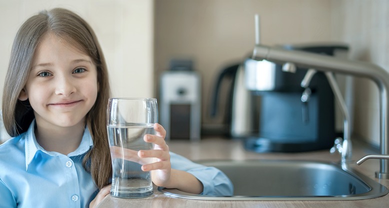 Girl next to kitchen sink holding a glass of clear water