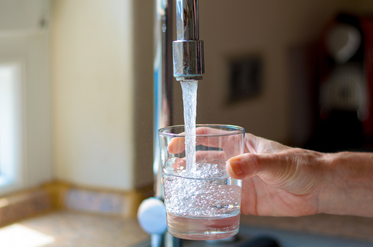 A person filling up a water glass with tap water from a kitchen faucet.